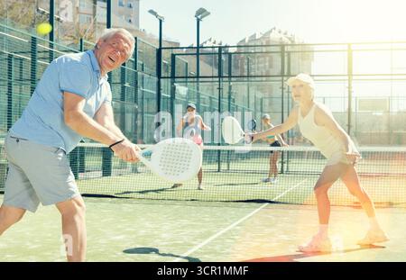 Motivierter Senior-Mann und -Frau spielen Padel mit seinem Teamkollegen vor Gericht Stockfoto