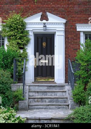 Backsteinhaus mit Weinstöcken und schwarzer Eingangstür Stockfoto