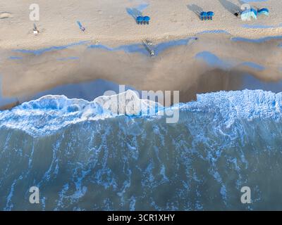Atemberaubende Luftaufnahme von Meereswellen, die bei Sonnenaufgang an einem Sandstrand brechen, mit lebendigem blauem Wasser und warmem goldenem Sand. Perfekt für Reisen, Urlaub Stockfoto