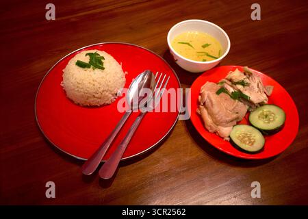 Ingkung Ayam, ein traditionelles Essen aus Yogyakarta, Indonesien, hergestellt aus einem gekochten Huhn, mit Reis und in Scheiben geschnittenen Gurken auf roten Tellern. Stockfoto