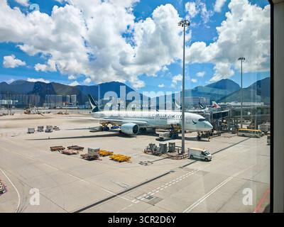 Hongkong, China - 13. September 2025 : geschäftige Flughafenszene in Hongkong: Ein kommerzieller Jet auf dem Asphalt, umgeben von Bodenunterstützung, mit Bergen und Stockfoto