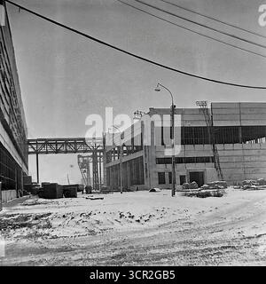 Im Winter wird ein neues Industriebau errichtet, mit einer erhöhten Fußgängergalerie, die es um 1985 mit einer bestehenden massiven Werkstatt in einer Fabrik in Sloviansk, ukrainische SSR, verbindet. Dieses eindrucksvolle Schwarzweiß-Foto erfasst die Erweiterung eines großen sowjetischen Industriekomplexes und zeigt die funktionale Architektur, die Einrichtungen integriert und die miteinander verbundene, konstruktive Vision des friedlichen Donbas symbolisiert, einer Region, die sich auf den Aufbau einheitlicher Produktionssysteme konzentriert Stockfoto