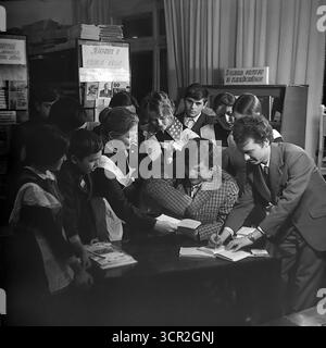 Eine Gruppe begeisterter Schulkinder in Uniform versammelt sich um einen Tisch mit ihren Lehrern und einem Gastautor oder einem Gastgast in einer Schulbibliothek in Sloviansk, Ukrainische SSR, um 1985. Dieses stimmungsvolle Schwarz-weiß-Foto fängt die Spannung eines literarischen Ereignisses ein, ein gemeinsamer Teil der sowjetischen Bildung, das die Bedeutung von Büchern und Lernen symbolisiert und den neugierigen, wissenssuchenden Geist der Jugend im friedlichen Donbass repräsentiert. Stockfoto