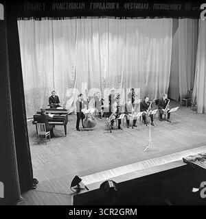 Eine sowjetische Jazzband mit Klavier, Kontrabass, Saxophonen und Posaunen, tritt auf der Bühne eines Kulturpalastes während eines Stadtfestes in Sloviansk, Ukrainische SSR, um 1985 auf. Dieses Schwarzweiß-Foto in Hochwinkel zeigt ein Live-Big-Band-Konzert, eine beliebte Unterhaltungsform in der UdSSR, das das reiche kulturelle Leben der Stadt zeigt und die fröhlichen, künstlerischen Feierlichkeiten symbolisiert, die Teil des Alltags in der friedlichen Donbass-Region waren. Stockfoto