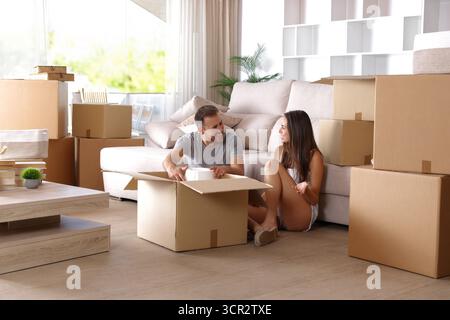 Glückliche Paare, die beim Umzug nach Hause reden und ihre Sachen auspacken Stockfoto