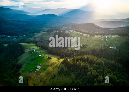 Blick aus der Vogelperspektive auf die ländliche Landschaft in der Ukraine, mit üppigen grünen Feldern, dichten Wäldern und verstreuten Häusern, eingebettet in sanfte Hügel. Die untergehende Sonne strahlt warmes Licht aus und sorgt für eine ruhige Atmosphäre. Stockfoto