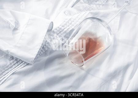 Glas, mit rosafarbenem Wein, verschüttet auf einem weißen Hemd, Nahaufnahme, selektiver Fokus, keine Leute, Konzept, Draufsicht Stockfoto