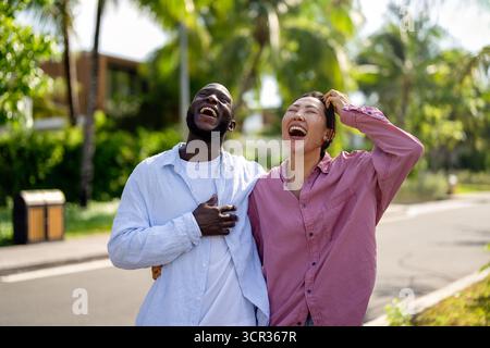 Glückliches, interrassisches Paar lacht zusammen draußen, genießt einen unbeschwerten Moment der Liebe, Freude Stockfoto