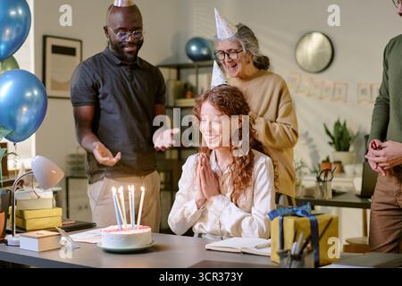 Junge Frau lächelt, während sie mit Freunden drinnen Geburtstag feiert Stockfoto