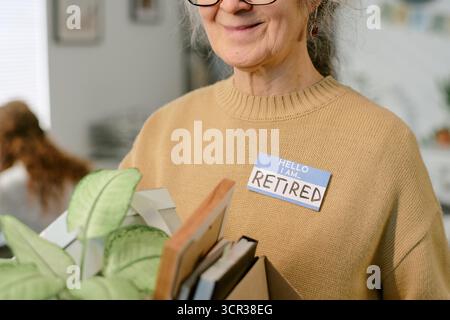 Eine ältere Frau lächelt, während sie nach dem Ruhestand Bürobedarf hält Stockfoto