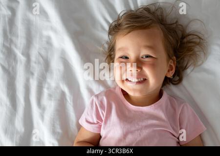 Lächelndes Mädchen, das auf weißen Bettlaken liegt Stockfoto