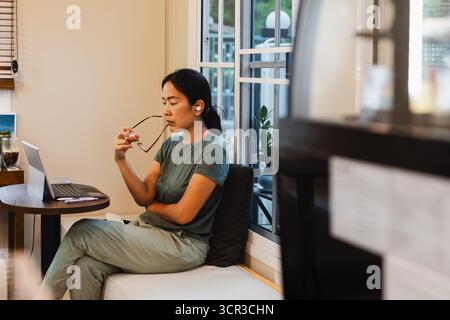 Nachdenkliche asiatische Frau, die an Laptop denkt und Probleme bei der Arbeit löst. Stockfoto