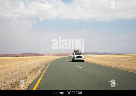 Im Inneren von Sossusvlei ziehen sich Schotterstraßen und ein Auto durch rote Dünen nach Deadvlei, Big Daddy und Sesriem Canyon, wo Sie malerische, staubige Wüstenausblicke genießen können. Nami Stockfoto