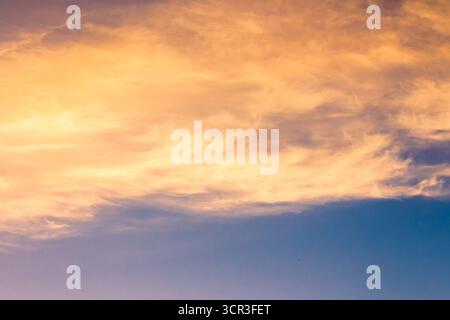 Orangefarbene Wolke am blauen Himmel bei Sonnenuntergang. Wunderschöner Naturhintergrund in der Abenddämmerung für Meteorologie. wolkenlandschaft in gelbem Licht. Abstrakte Szene des Sommerwetters Stockfoto