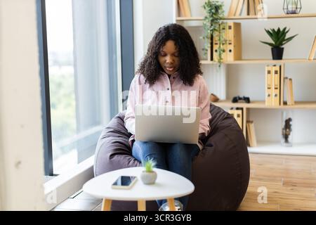 Junge Frau, die an einem Laptop in einem gemütlichen, modernen Zuhause arbeitet Stockfoto