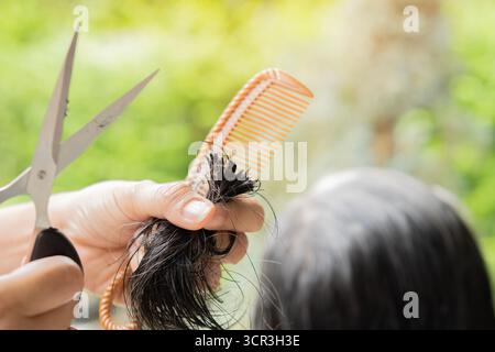 Der Friseur macht einen Haarschnitt für eine ältere Frau in der Natur zu Hause. Der Friseur schneidet nasse Haare und kämmt sie mit einem Kamm. Rückansicht. Stockfoto