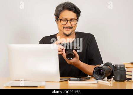 Porträt eines fröhlich lächelnden Erwachsenen Fotografen, der an einem Schreibtisch sitzt und eine Kamera in einem modernen Bürostudio hält. Stockfoto