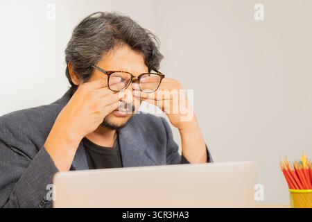 Augenproblem Konzept, Ermüdung asiatischer erwachsener Mann müde Augen, gereizt Reibung Auge trockene Linderung Sehschmerzen nach der Arbeit am Laptop, Augenbelastung, während des Tragens Stockfoto