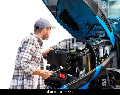 Männlicher Mechaniker mit digitalem Tablet in der Nähe des Traktors mit offener Haube isoliert auf weißem Hintergrund. Stockfoto