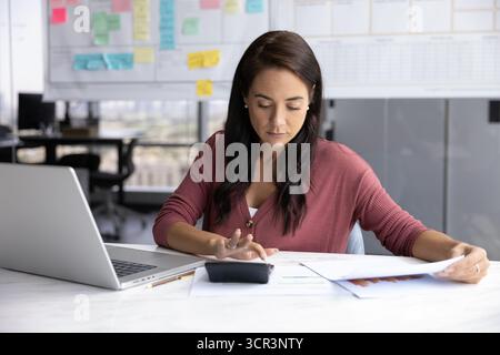 Frau, die an Berechnungen arbeitet, sitzt am Schreibtisch mit Rechnungen Stockfoto