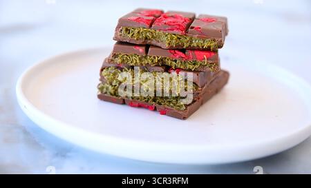 Die virale Dubai Kunafa Chocolate Bar, die auf einem wunderschönen weißen Teller mit weißem Hintergrund präsentiert wird und in zwei Stücke geteilt ist, sieht unwiderstehlich lecker aus Stockfoto