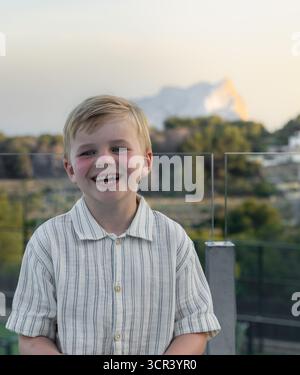 Lächelnder Junge in weißem Hemd, der draußen im Abendlicht steht Stockfoto