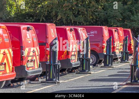 Eine Reihe roter Royal Mail-Transporter, die an mehreren festen Ladestationen in einem Royal Mail-Büroparkplatz aufgeladen werden. Stockfoto