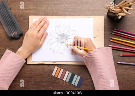 Frau zeichnet eine Zeichnung von Blumen am Holztisch, Draufsicht Stockfoto