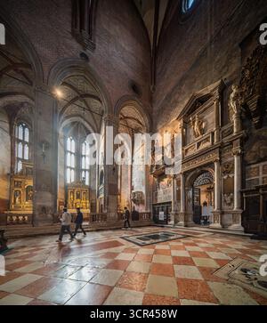 Sakristentor und Apsiskapellen in Santa Maria dei Frari, Venedig. Geschnitzter Stein und vergoldete Altäre leuchten unter geriffelten Gewölben und gefiltertem Licht. Stockfoto