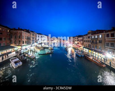 Lange Sicht zeigt den lebhaften Canal Grande in Venedig, mit Lichtern, die auf dem Wasser reflektieren und die Menschen genießen die lebhafte Atmosphäre der Dämmerung. Stockfoto