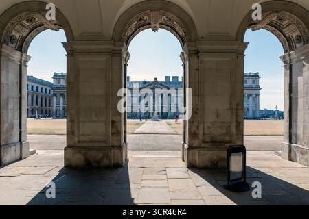 Historische Bögen, die ein klassisches Gebäude in einem sonnendurchfluteten Innenhof umrahmen. Maritime Greenwich, London, Vereinigtes Königreich Stockfoto