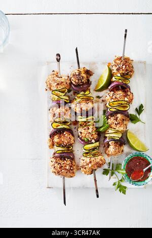 Gegrillte Hähnchenspieße mit Zucchini, Limettenscheiben und Sauce auf weißem Hintergrund. Stockfoto