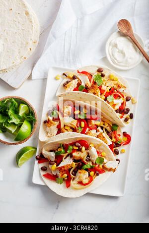 Tacos mit gegrilltem Huhn, Mais, Bohnen, roter Paprika und Kräutern auf einem weißen Teller. Stockfoto