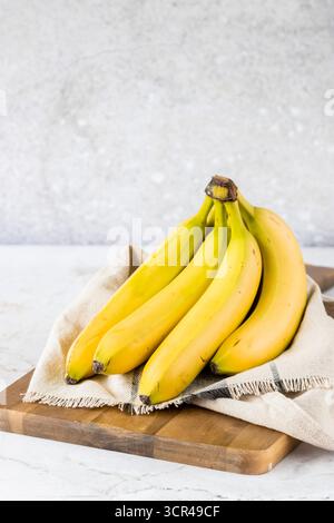 Reife gelbe Bananen auf einem rustikalen Holzbrett mit Tuch angeordnet, im Stil einer tropischen Frucht und gesunder Ernährung. Stockfoto