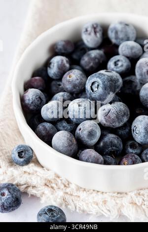 Nahaufnahme reifer Heidelbeeren in einer weißen Keramikschale auf Leinen, gestylt als gesundes Superfood- und Fruchtkonzept. Stockfoto