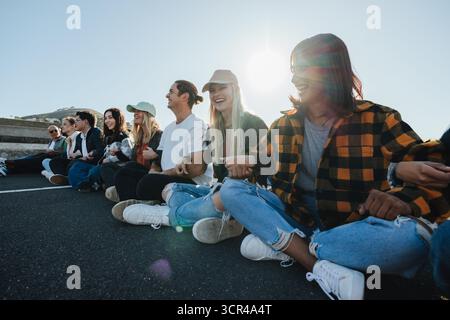 Eine vielfältige Gruppe junger Erwachsener, die an einem friedlichen Protest im Freien teilnehmen, während sie gemeinsam auf einer Straße sitzen. Die Atmosphäre vermittelt das Stockfoto