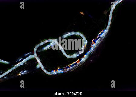 Nächtliche Luftaufnahme der kurvenreichen Straße mit farbenfrohen Fahrzeuglichtern in einer dunklen Landschaft. Kelok 9 oder die 9 Haarnadeln, Harau, West Sumatra, Indonesien Stockfoto