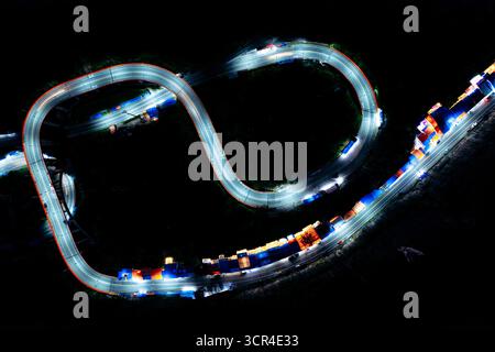 Nächtliche Luftaufnahme der kurvenreichen Straße mit farbenfrohen Fahrzeuglichtern in einer dunklen Landschaft. Kelok 9 oder die 9 Haarnadeln, Harau, West Sumatra, Indonesien Stockfoto