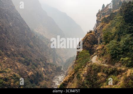 Nebliges Bergtal mit zerklüfteten Klippen und einem gewundenen, schmalen Pfad entlang des Hügels. Straße F36 von Annapurna in der Provinz Gandaki, Nepal Stockfoto