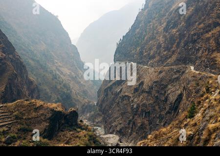 Ein zerklüfteter Bergpfad schlängelt sich durch hoch aufragende Klippen unter einem nebeligen Himmel in einer abgelegenen Landschaft. Straße F36 von Annapurna in der Provinz Gandaki, Nepal Stockfoto
