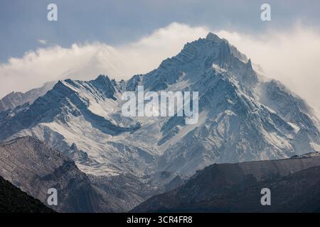 Schneebedeckte Berge mit zerklüfteten Gipfeln erheben sich majestätisch unter einem bewölkten blauen Himmel. F042, Annapurna, Mustang District, Provinz Gandaki, Nepal Stockfoto