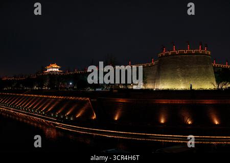 Antike Stadtmauer, beleuchtet bei Nacht mit dekorativen Lichtern und einem ruhigen Graben darunter. XI'an, China Stockfoto