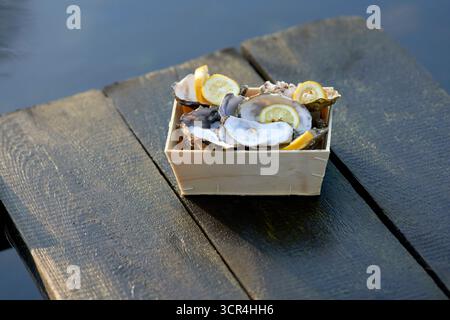 Frisch gegessen geschuckte Austern in einer Holzkiste mit Zitronenscheiben auf einer rustikalen Holzoberfläche. Stockfoto
