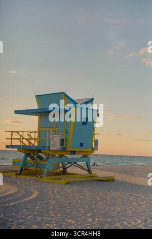 Ein farbenfroher Rettungsschwimmer-Turm an einem ruhigen Strand bei Sonnenuntergang, der lange Schatten auf den Sand wirft. Miami, Florida, USA Stockfoto