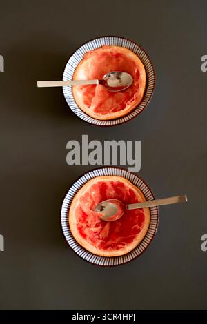 Zwei Grapefruithälften mit Löffeln auf einer dunklen Oberfläche, von oben gesehen. Stockfoto
