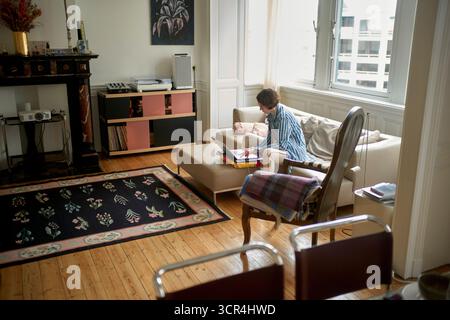Eine Frau mit gestreiftem Hemd sitzt auf einem Sofa und arbeitet an einem Laptop in einem gemütlichen Wohnzimmer. Brüssel, Belgien Stockfoto
