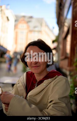 Frau in einem beigefarbenen Mantel sitzt draußen mit einer verschwommenen Stadtstraße im Hintergrund. Brüssel, Belgien Stockfoto
