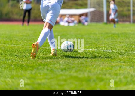 Nahaufnahme eines jungen Fußballspielers in weißer Uniform, der Ball auf dem Feld tritt. Stockfoto