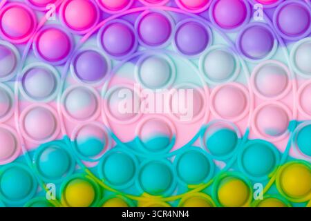 Lebendige Nahaufnahme eines Regenbogen-Pop-it-Fidget-Spielzeugs mit rosa, lila, türkisfarbenen und gelben Blasen in einem abstrakten, verspielten Arrangement. Stockfoto