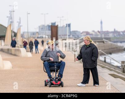 Ein älterer Mann und eine ältere Frau an der modernen Promenade in Edinloys, Lancashire, Großbritannien. Der Mann fährt einen Mobilitätsroller Stockfoto